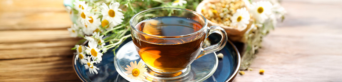 Foto de una taza con té de manzanilla sobre un plato con flores de manzanilla en el fondo